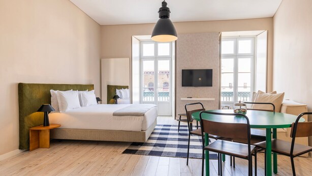 Habitación de hotel con cama, escritorio, mesa de comedor con sillas, televisión y ventanas amplias.