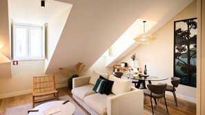 Een knus loft-achtig woongedeelte met een hoge plafond, een eethoek en een groot raam.