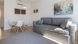 Un salon moderne avec un canapé gris, une table à manger avec des chaises et une œuvre d’art géométrique accrochée au mur.