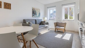 Un salon moderne avec un canapé gris, une table à manger avec des chaises, un tapis gris et une vue sur la ville par les fenêtres.