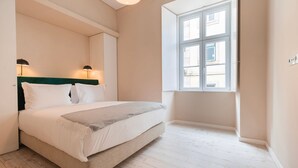 Ett sovrum med en säng, två sänglampor, ett fönster och en grön sänggavel.