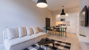 A modern living room with a sofa, a small table, and a checkered rug. There is a kitchen area with a dining table and chairs, a microwave, and a chalkboard. - Carmo 43 | Apartamento 104 (Lisboa)
