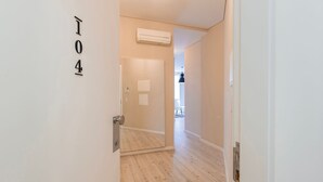 A hallway with a door labeled "104" leading to a room with a wooden floor and a ceiling-mounted air conditioner. - Carmo 43 | Apartamento 104 (Lisboa)