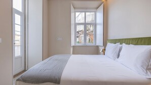 A bedroom with a bed, a window, and a view of the outside. - Carmo 43 | Apartamento 104 (Lisboa)
