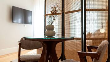 Un comedor moderno con una mesa redonda de cristal, dos sillas tapizadas y un jarrón decorativo con ramas.