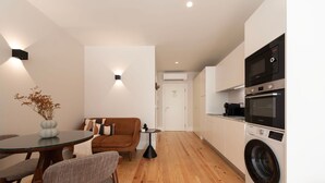 A compact living space with a kitchenette, a dining area, and a sofa. - Ando Living - Flores 200 Townhouse - 102 (Porto)