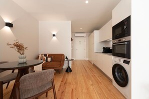 A compact living space with a kitchenette, a dining area, and a sofa. - Ando Living - Flores 200 Townhouse - 102 (Porto)