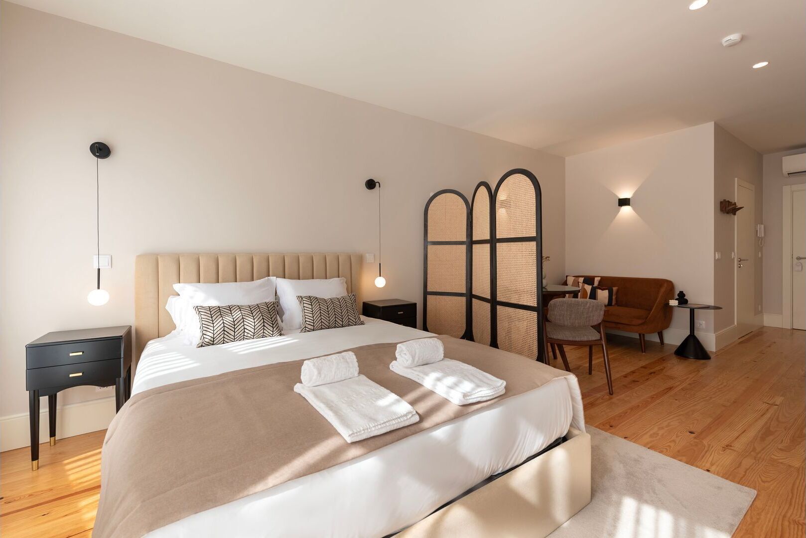 Un dormitorio moderno con una cama grande, mesitas de noche, una zona de estar con un sofá y un sillón, y un mamparo.