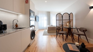 A modern apartment with a kitchen, dining area, and living space. It includes a washing machine, a dining table with chairs, and a sofa. - Ando Living - Flores 200 Townhouse - 102 (Porto)
