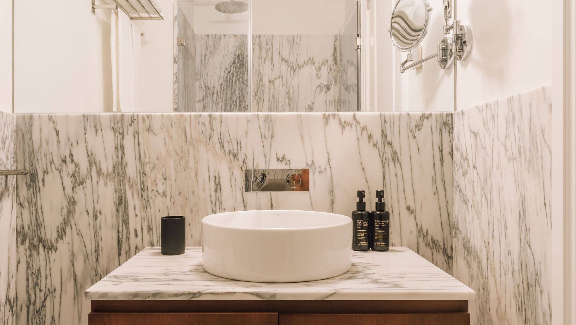 Ein Badezimmer mit Waschtisch aus Marmor, einem runden Becken, einem Handtuchhalter und zwei Shampoo-Flaschen.