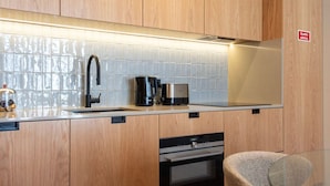 A modern kitchen with wooden cabinets, a stainless steel range hood, a coffee maker, and a built-in oven. - Ando Living - Santa Catarina Townhouse - 102 (Porto)