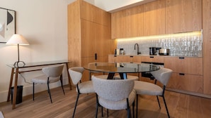 A modern kitchen with wooden cabinets, a glass-top dining table, and a coffee maker. - Ando Living - Santa Catarina Townhouse - 102 (Porto)