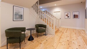 Een modern interieur met een trap, twee groene fauteuils, een klein rond tafeltje en ingelijste kunstwerken aan de muren.