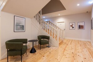 Ein modernes Interieur mit einer Treppe, zwei grünen Sesseln, einem kleinen runden Tisch und gerahmten Kunstwerken an den Wänden.