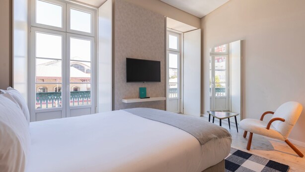 A hotel room with a large bed, a TV mounted on the wall, a small table, and a chair. - Carmo 43 | Apartamento 201 (Lisboa)