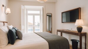 Ein Hotelzimmer mit Bett, Nachttisch, Lampe, Spiegel und Blick auf die Stadt durch das Fenster.