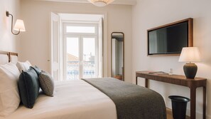 A hotel room with a bed, bedside table, lamp, mirror, and a view of the city through the window. - Ando Living - Abrantes 50 House - 501 (Lisbon)