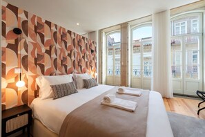 Une chambre d’hôtel avec un grand lit, un mur décoré de motifs et un balcon offrant une vue sur les immeubles.