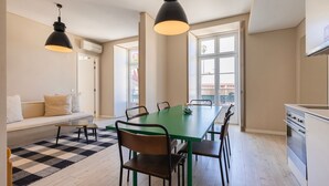 Et moderne køkken med spiseplads, med et grønt bord, sorte stole og hængende lamper.