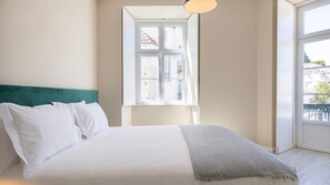 A bedroom with a bed, white bedding, a teal headboard, and a window with a view of buildings. - Carmo 43 | Apartment 202 (Lisboa)