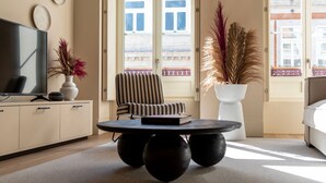 A modern living room with a TV, striped armchair, round coffee table, and decorative plants. - Ando Living - Santa Catarina Townhouse - 201 (Porto)