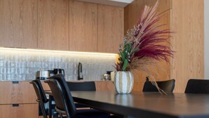 A modern kitchen with wooden cabinets, a striped vase with dried plants, and a dining table with chairs. - Ando Living - Santa Catarina Townhouse - 201 (Porto)