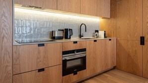 A modern kitchen with wooden cabinets, a stainless steel range hood, a built-in oven, and a black coffee maker. - Ando Living - Santa Catarina Townhouse - 201 (Porto)