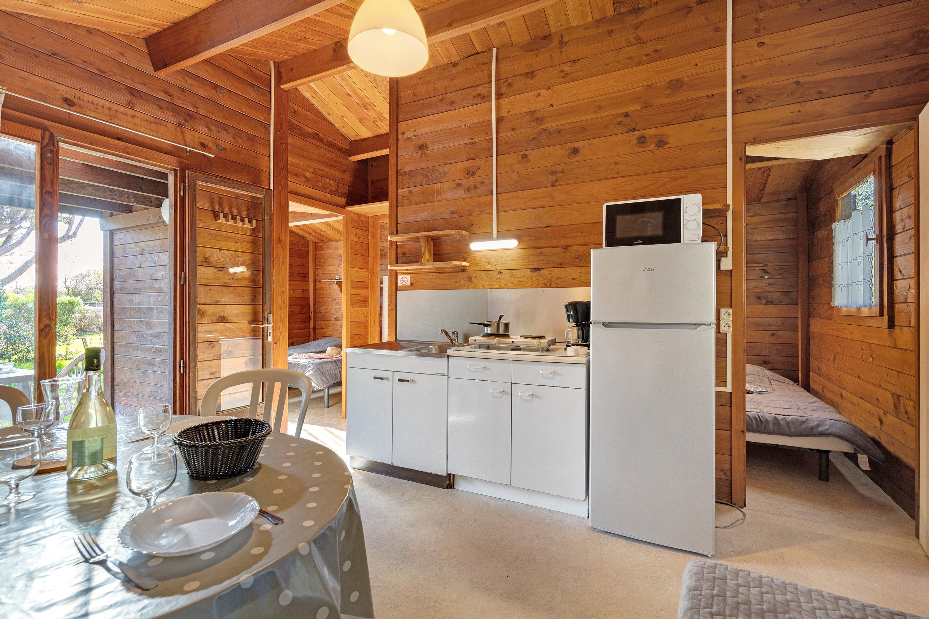 Ein gemütliches Holzhaus mit einer Küchenzeile, einem Essbereich mit Tisch für zwei Personen und einem Bett in der Ecke.