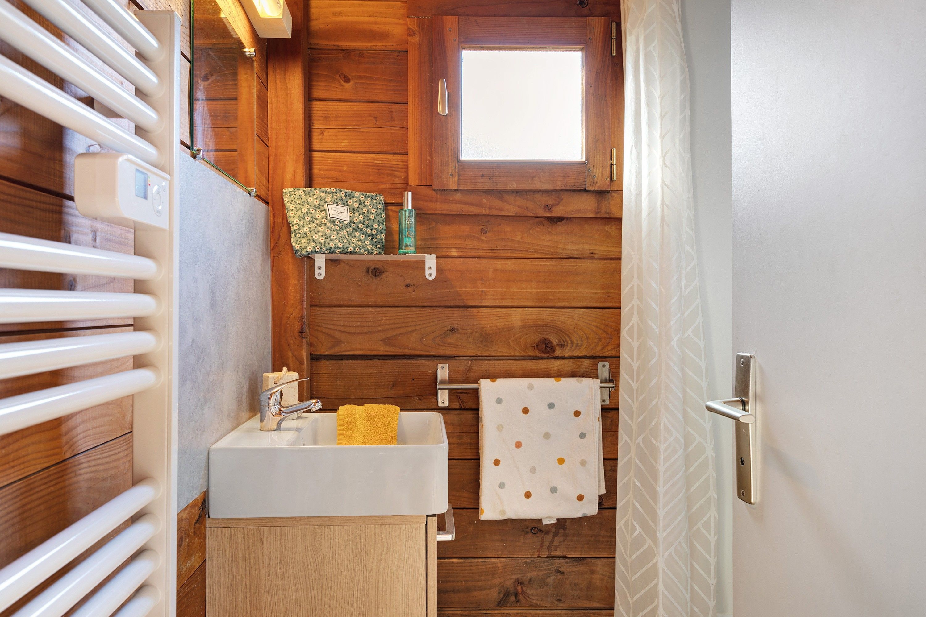 A bathroom with wooden walls, a white sink, a towel rack, and a window.
