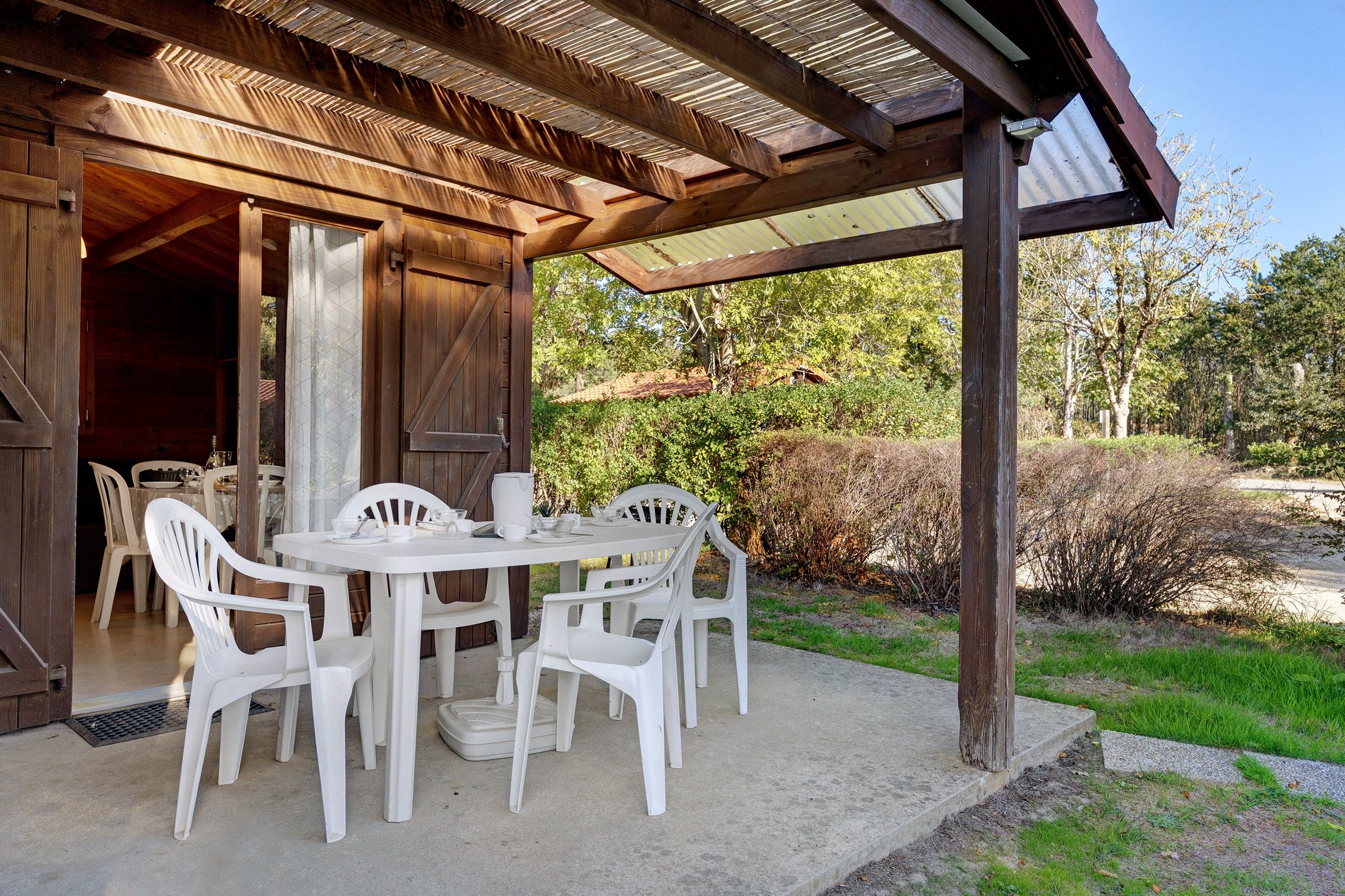 Eine Außenpatio mit einer Holz-Pergola, weißen Plastikstühlen und einem für das Essen gedeckten Tisch.