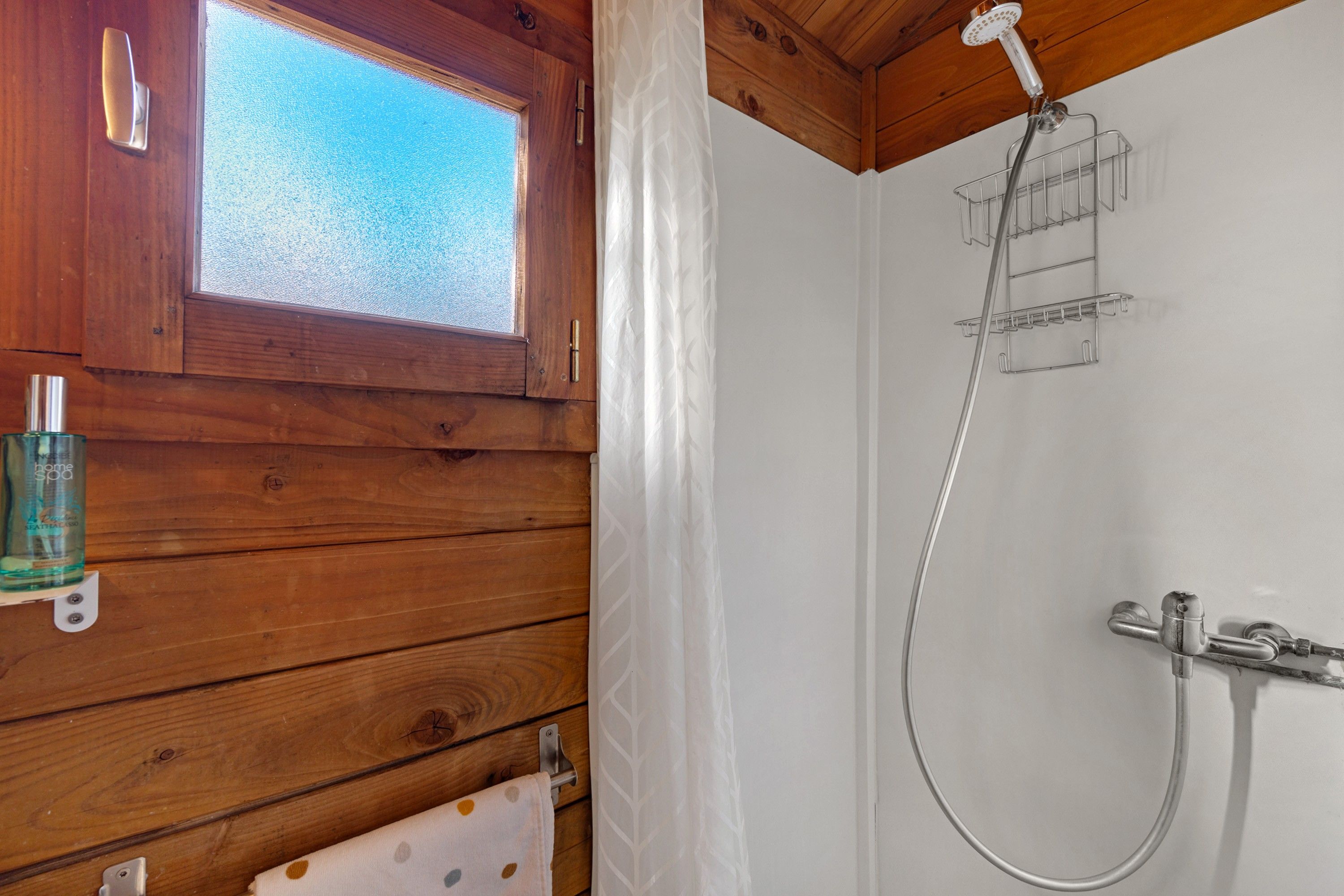 Innenansicht einer Holzhütte mit Dusche, einem Fenster und einer Shampoo-Flasche.