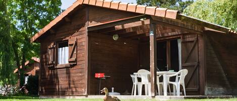 A rustic wooden cabin with a covered porch, a table, and chairs.