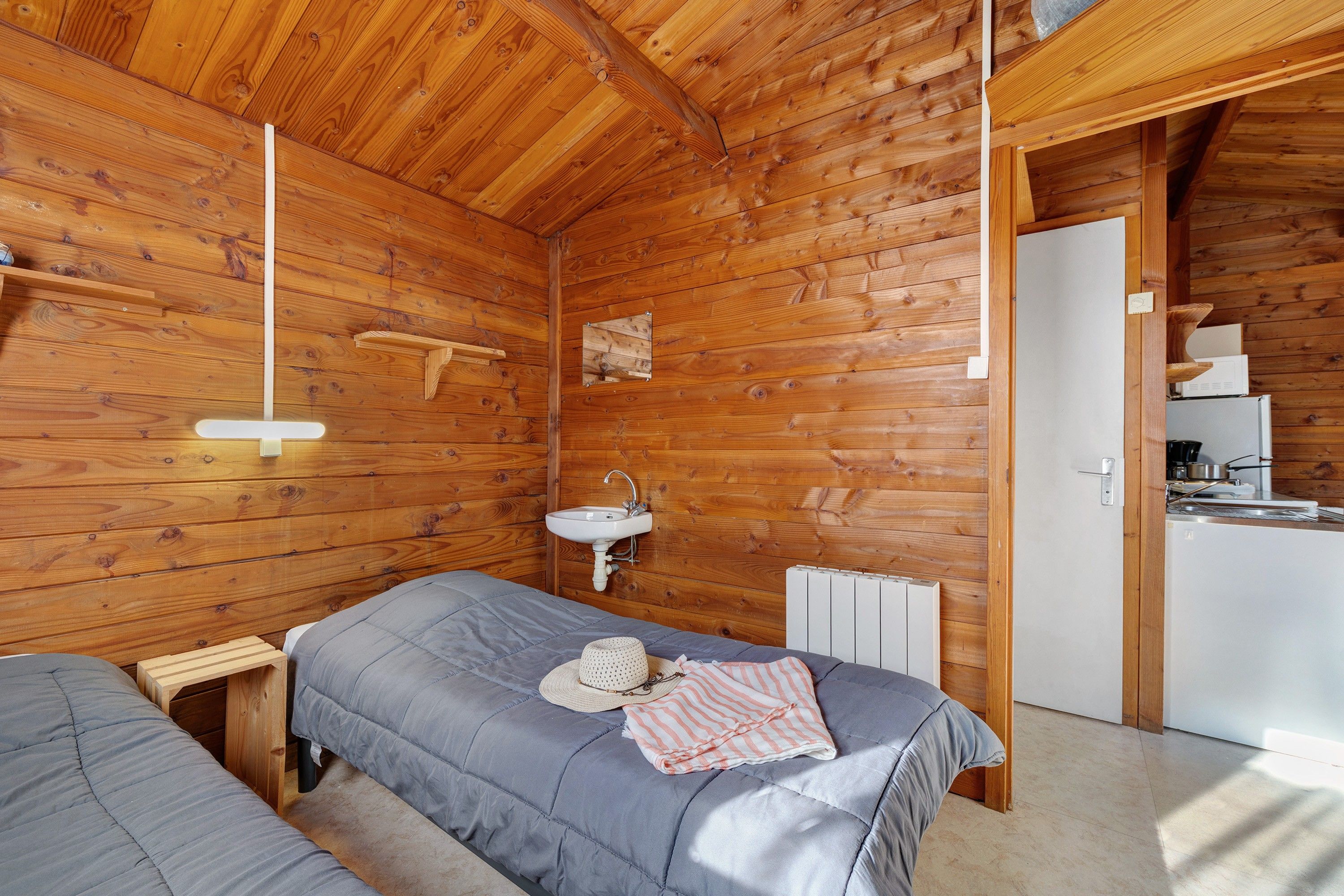 Una cabaña de madera acogedora con una cama individual, un lavamanos integrado y una pequeña cocina.