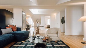 Ein modernes Wohnzimmer mit Sofa, Sessel, Couchtisch und einem Essbereich im Hintergrund.