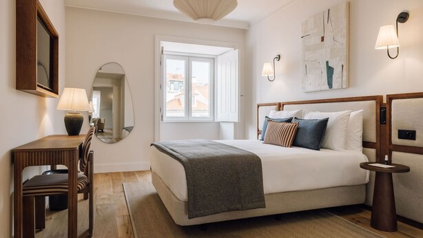 Ein Hotelzimmer mit Bett, Nachttisch, Lampe, Spiegel und einem Fenster mit Aussicht.