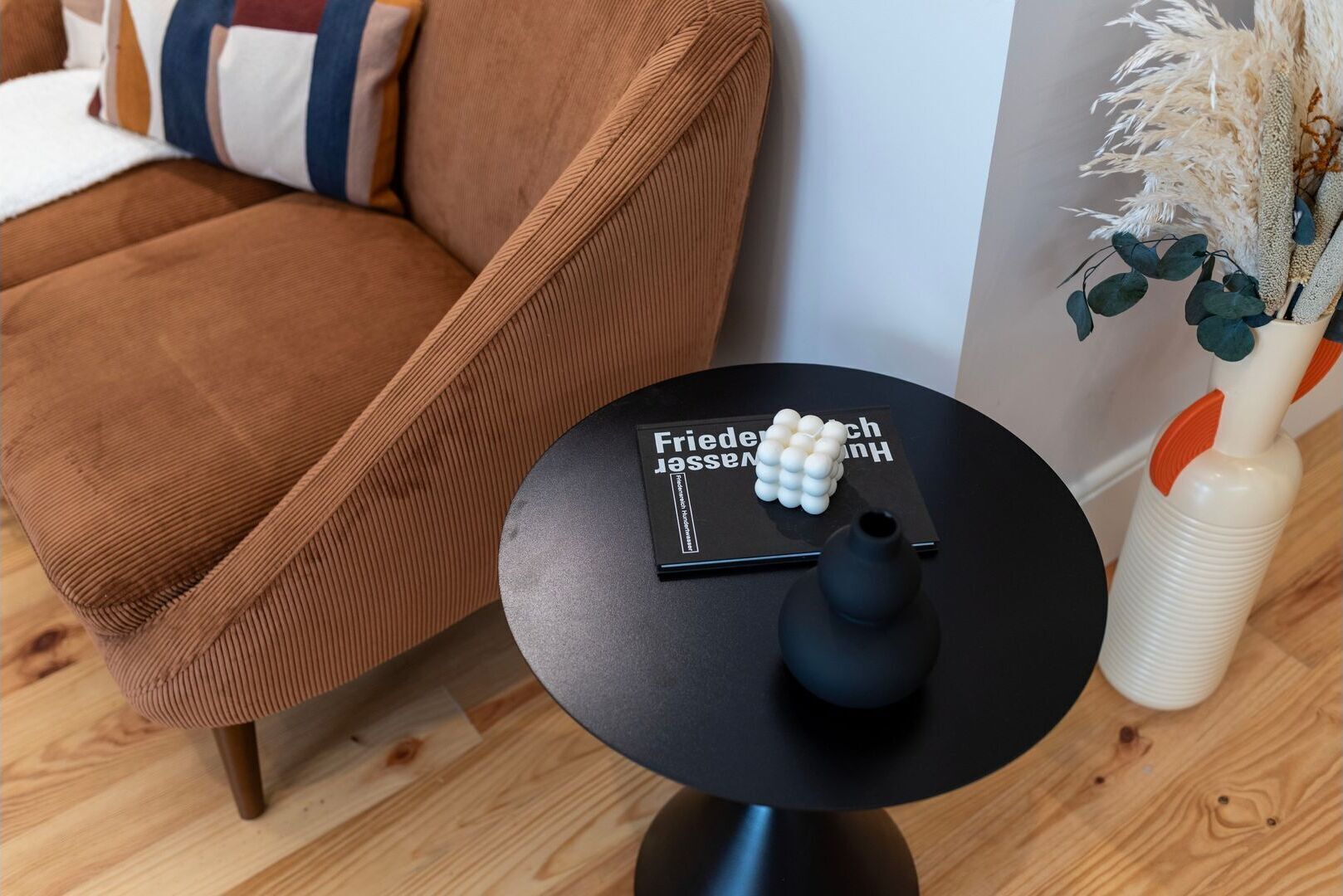 Un salon moderne avec un canapé marron, une table ronde noire sur laquelle se trouvent un livre et un vase, ainsi qu’une plante décorative.