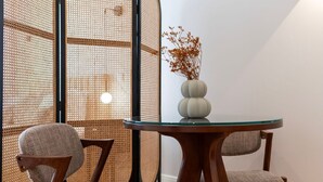 Una habitación con una mesa redonda de cristal, dos sillas de madera y un jarrón blanco con flores secas.