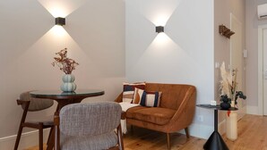 Una sala de estar moderna con un sofá marrón, dos sillones, una mesa de centro de vidrio y un jarrón con plantas secas.