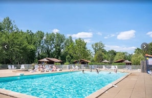 A swimming pool with lounge chairs and umbrellas, surrounded by trees.