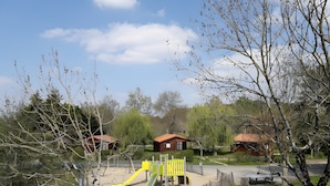 Un parque infantil con toboganes y un área cercada, rodeado de árboles y edificios.