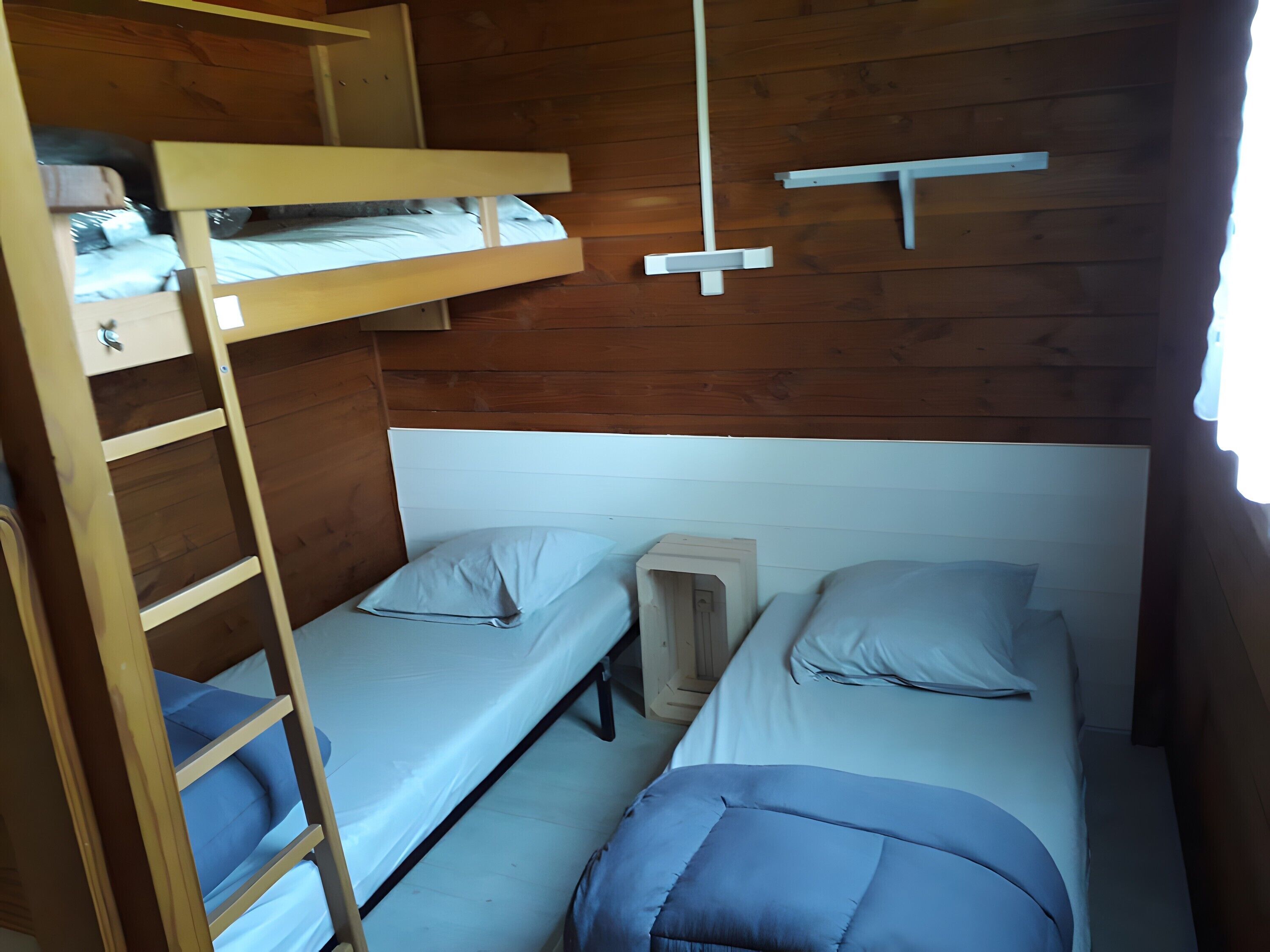 A bunk bed room with two beds, a wooden ladder, and a small shelf.