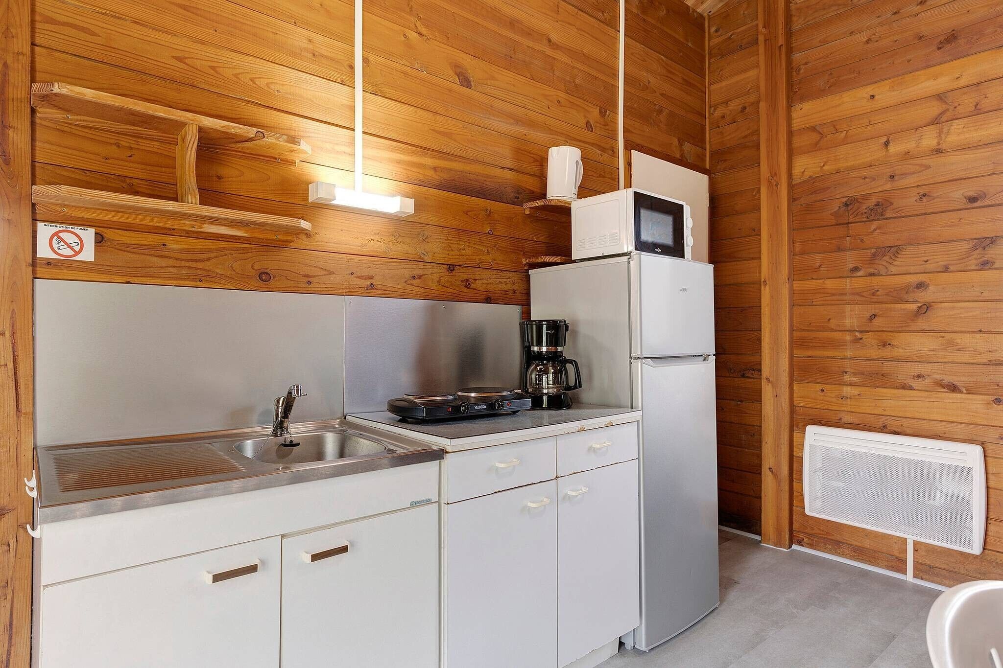 Una cocina compacta con un lavamanos de acero inoxidable, cafetera, microondas y refrigerador.
