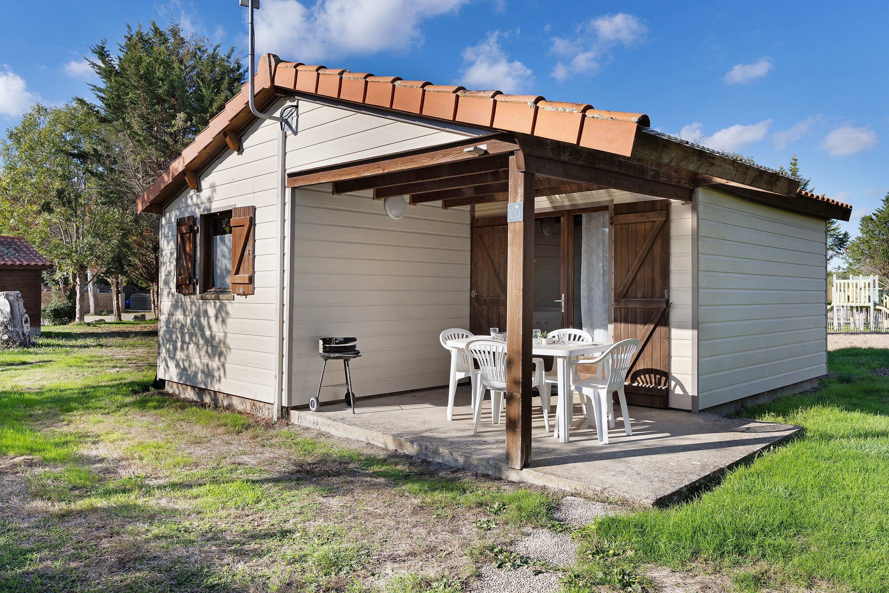 Un petit bâtiment d’un seul étage, doté d’un porche abrité, d’une table avec des chaises et d’un barbecue à l’extérieur.