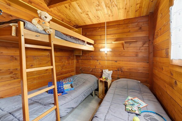 A wooden cabin room with bunk beds, a ladder, a small table with a teddy bear, and a window with curtains. - Chalet “Bois 3” with Shared Pool and Private Terrace (Saint-Gervais)