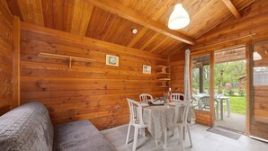 Un intérieur en bois comprenant un canapé, une table à manger, des chaises et une vue à travers une porte vitrée.