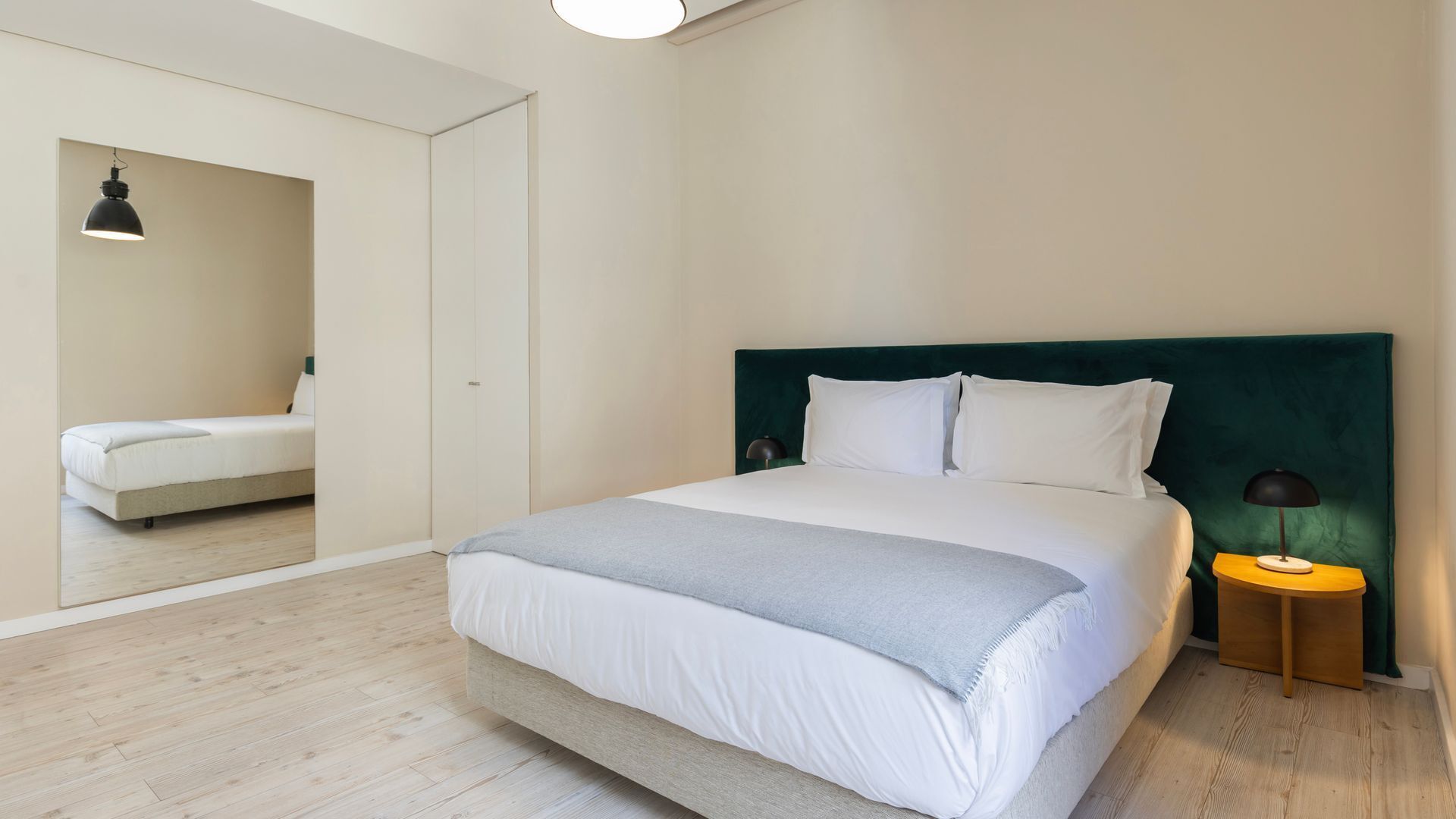 Ein Schlafzimmer mit einem Bett, einem Nachttisch, einer Lampe, einem Spiegel und einem Kleiderschrank.