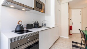 A modern kitchen with a built-in microwave, kettle, toaster, and coffee maker. There is a sink and a small dining area with a table and chair. - Carmo 43 | Apartment 203 (Lisboa)