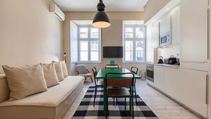 A compact kitchen with a dining table, chairs, a sofa, and a TV mounted on the wall. - Carmo 43 | Apartment 203 (Lisboa)