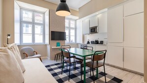A compact living space with a kitchenette, a dining area with a checkered rug, a sofa, and a TV mounted on the wall. - Carmo 43 | Apartment 203 (Lisboa)