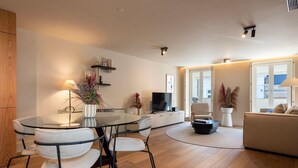Un salon moderne doté d’une table à manger en verre, de sièges confortables, d’un téléviseur à écran plat et d’une grande fenêtre offrant une vue sur la ville.
